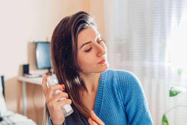 Young woman applying hair oil spray on hair at home.