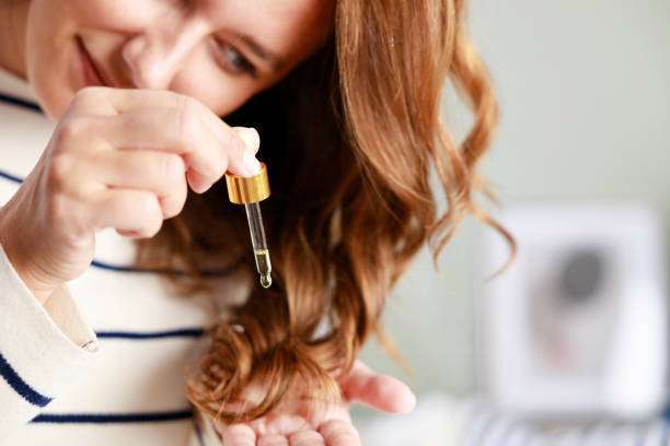A lady dripping hair oil with a pipette on her hair.