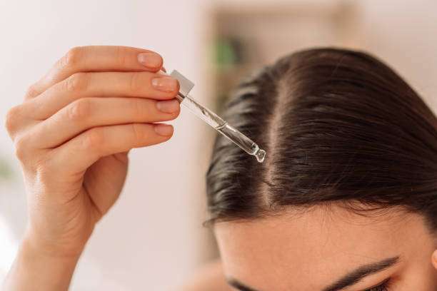 A lady dripping hair oil with a pipette on her hair.