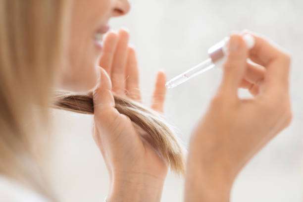 A lady dripping hair oil with a pipette on her hair.