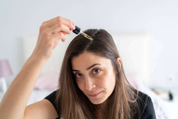 A lady dripping hair oil with a pipette on her hair.
