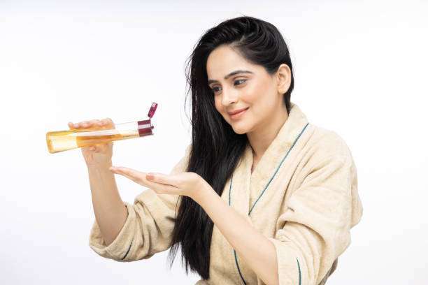 A lady dripping hair oil with a pipette on her hair.