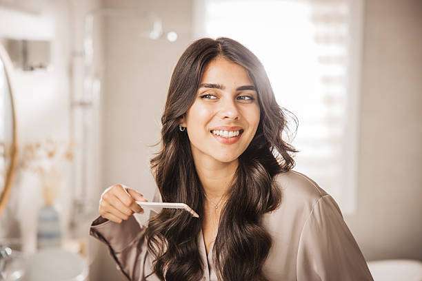 A lady dripping hair oil with a pipette on her hair.