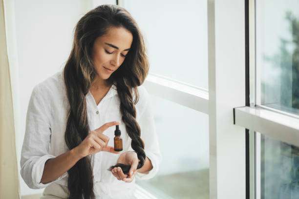 Woman applying hair oil to her long braided hair.