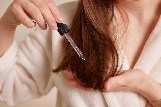 Woman applying hair oil with dropper to brown hair