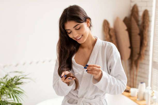 Woman applying hair oil to her healthy, long hair.