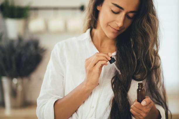 Woman applying hair oil with a dropper to her long, dark, wavy hair.