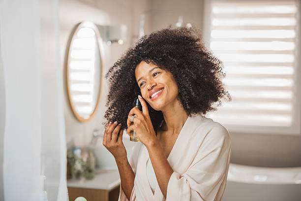 Happy young woman in bathrobe styling her hair oil in front of mirror in bathroom