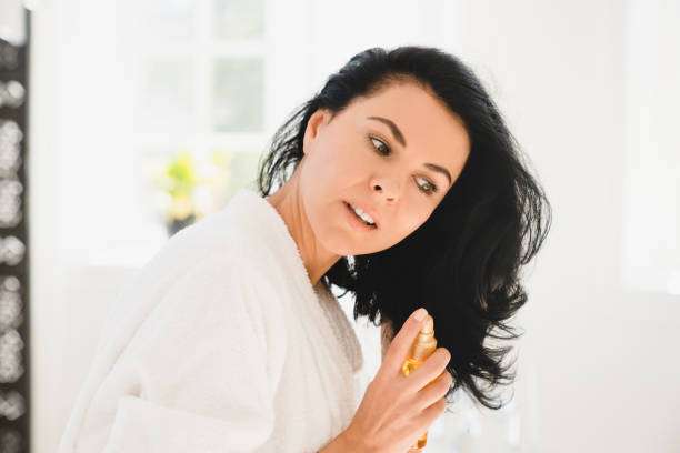 A middle-aged Caucasian woman applying a hair oil beauty mask on her long hair for care and treatment.