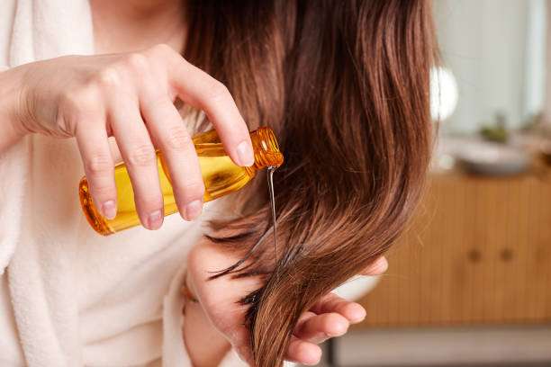 Woman applying hair oil to her healthy, long hair.
