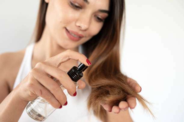 Woman applying hair oil to her healthy, long hair.