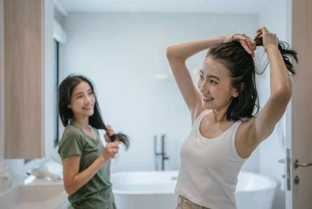 Young female adult standing in front of mirror in the bathroom at home after washing her hair oil