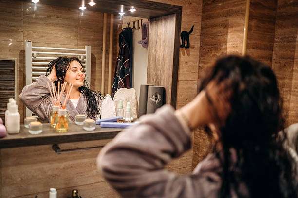 Young female adult standing in front of mirror in the bathroom at home after washing her hair oil