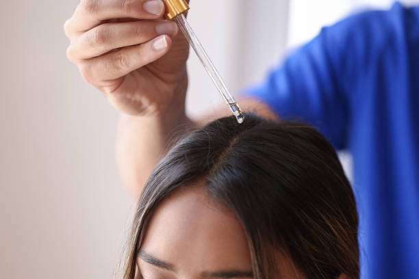 Applying hair oil directly to the scalp with a dropper for deep nourishment.