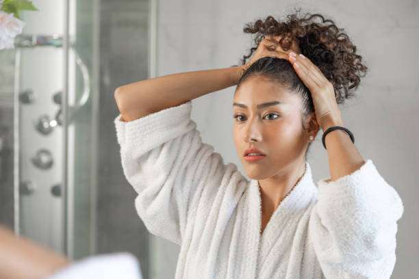 Woman in bathrobe styling curly hair up with hands.