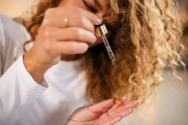 Woman applying nourishing hair oil drops to her curly hair strands.