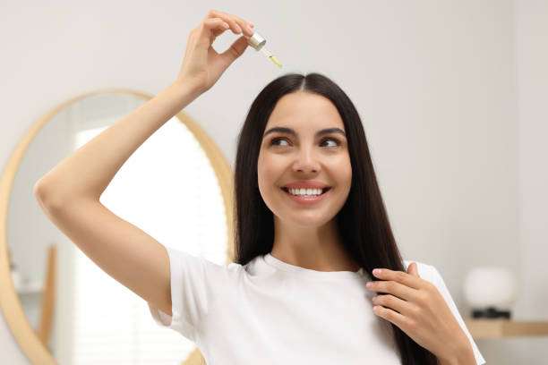 Young woman uses dropper for hair oil application.
