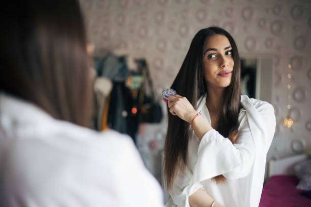 Woman admiring her long, healthy hair in mirror, enhanced by hair oil.