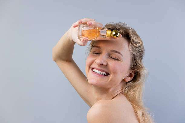 A stunning woman with long, flowing hair joyfully applies hair oil while beaming with happiness.