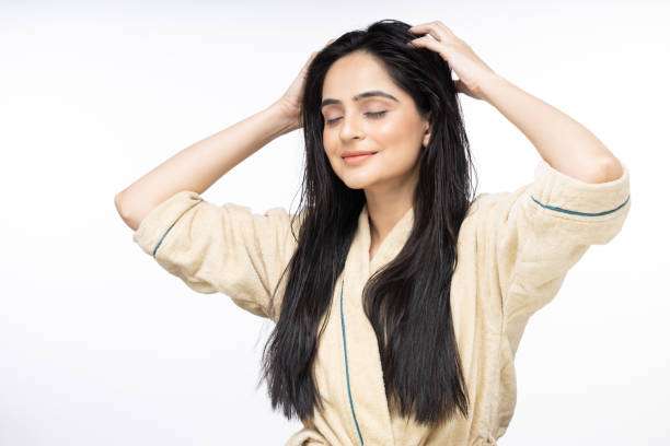Smiling woman massaging her wet hair and scalp, enjoying the benefits of hair oil.