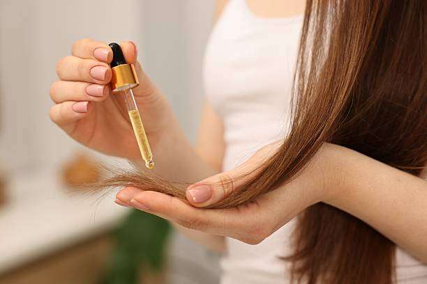 Close up of hand holding hair oil dropper to hair strand.