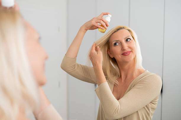 Blonde woman applying hair oil to her roots in mirror