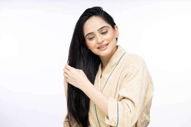 Woman in robe applies nourishing hair oil to long strands.