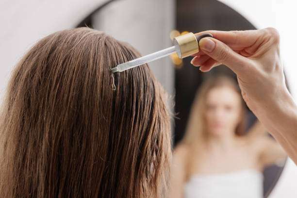 Hand applying nourishing hair oil to a woman's scalp with a dropper for treatment.