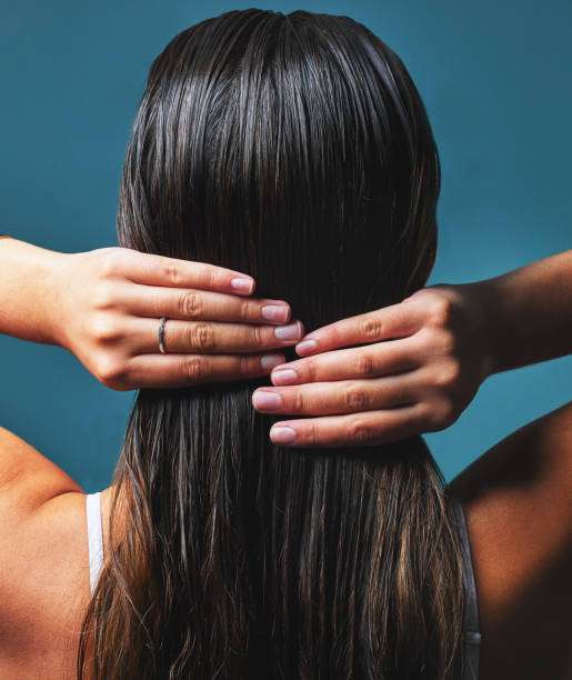 Woman applying hair oil to her healthy, long hair.