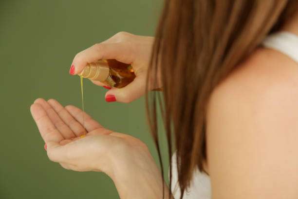 Woman dispensing golden hair oil into her palm, preparing for application to hair.