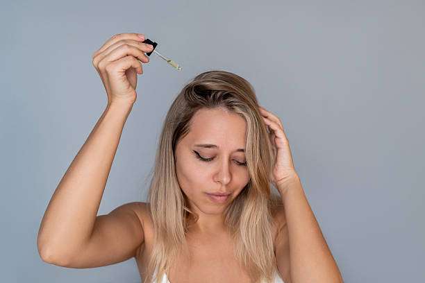 Blonde woman applying hair oil to scalp for growth and strength.