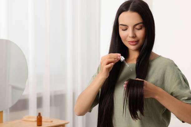 Brunette applying hair oil with dropper to long dark hair