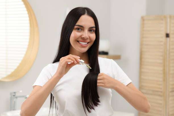 Woman applying hair oil to her healthy, long hair.
